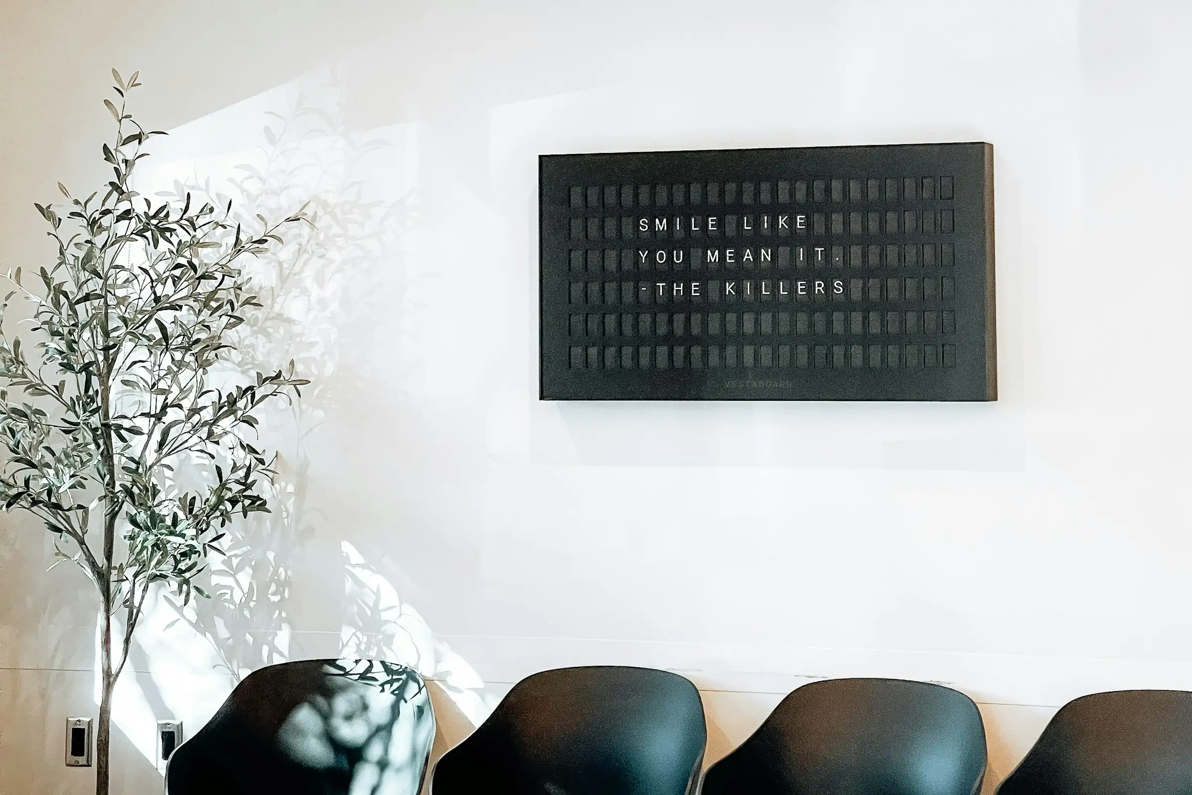 A clinic waiting room with black chairs and a letter board on the wall