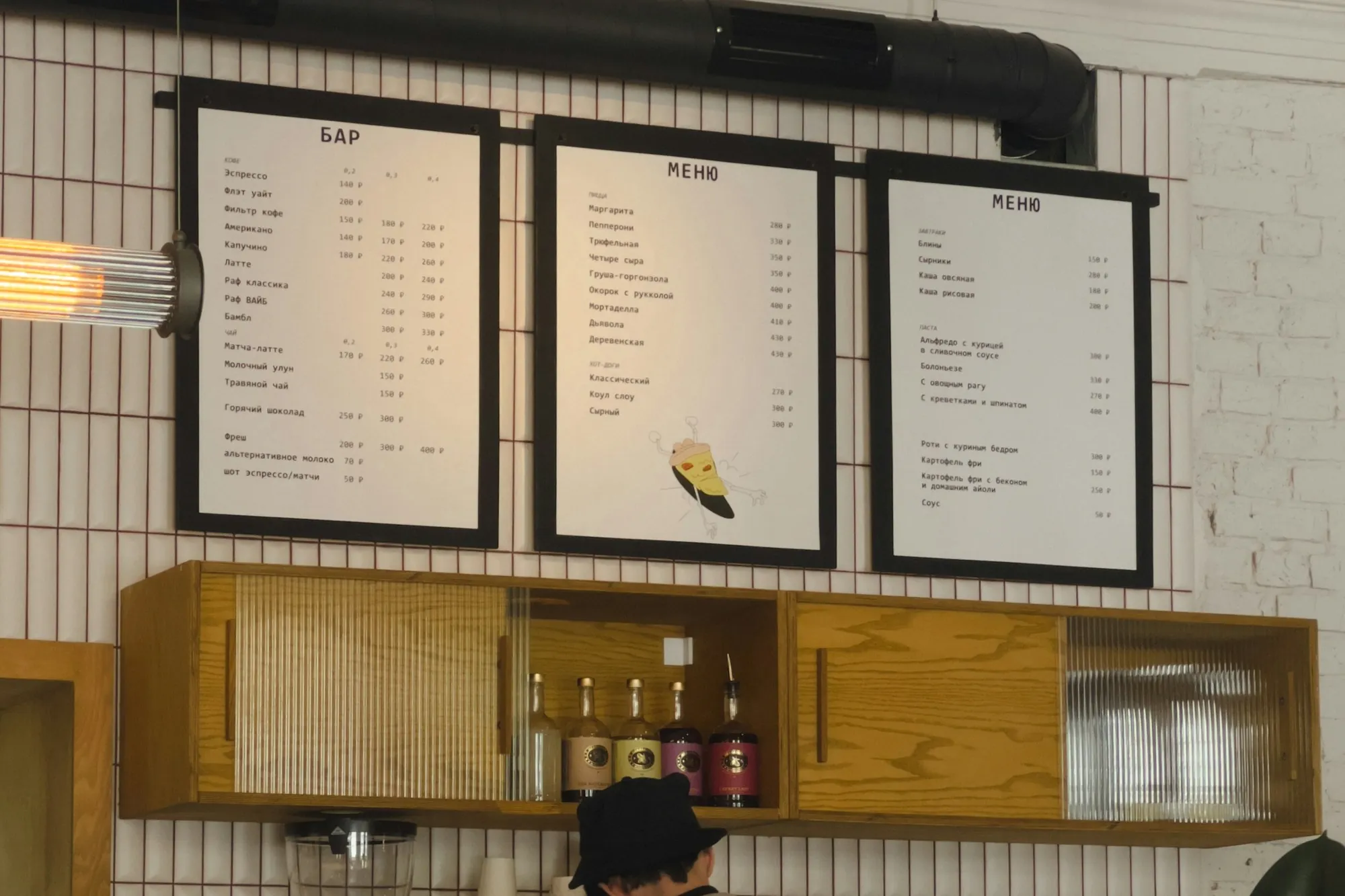 A café counter with three framed printed menus on the wall above it