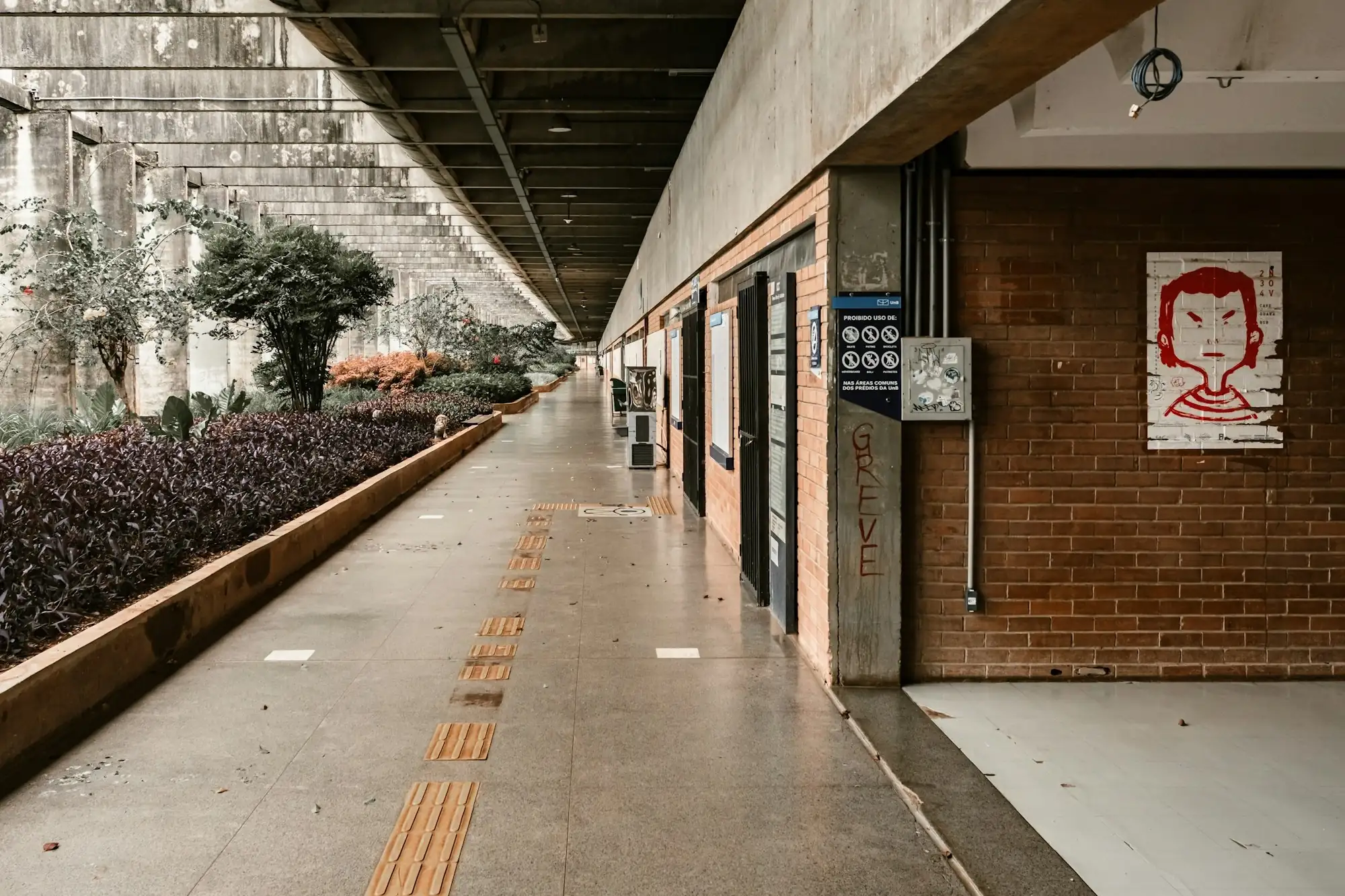 A covered school walkway with a painted poster on a brick wall and a sign on a concrete pillar
